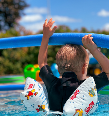 junge in neoprenanzug mit schwimm-nudel über dem kopf