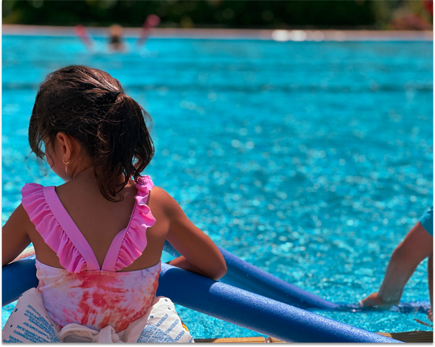 Mädchen sitzt an Poolkante und hat Schwimmnudeln in der Hand