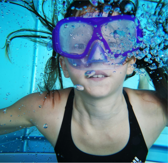 Mädchen Unterwasser mit Taucherbrille, es steigen Luftblasen auf